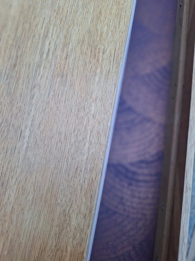 Vue rapprochée d'une planche de bois avec une surface texturée, montrant aussi un fond coloré en dessous.