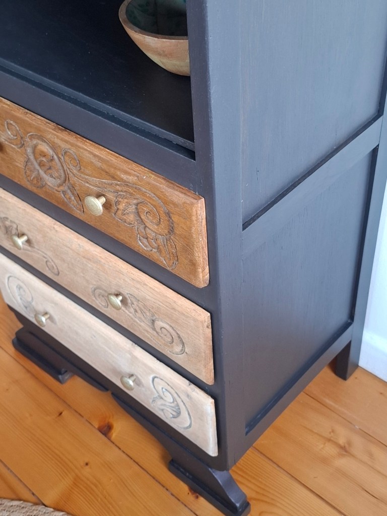 Meuble en bois avec tiroirs décorés, sur un sol en bois naturel.