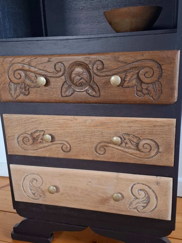 Tiroir en bois avec des motifs sculptés, mélange de teintes claires et foncées, et boutons en laiton.