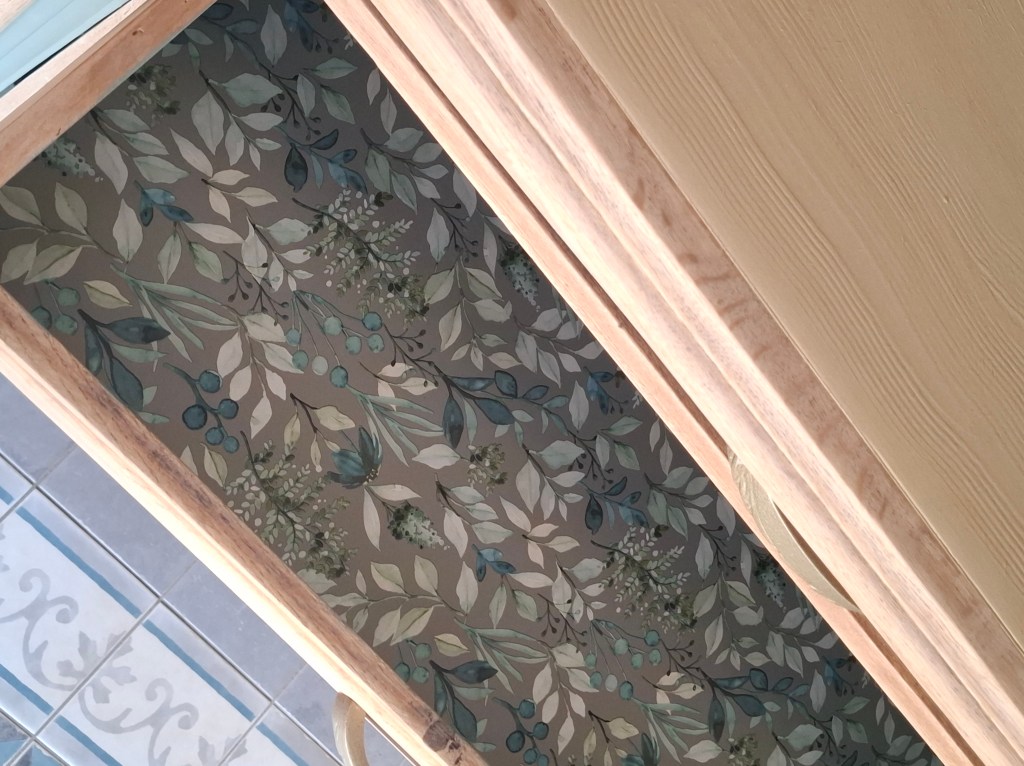 Intérieur d'un tiroir en bois avec un fond décoratif illustrant des feuilles et des baies dans des couleurs douces.