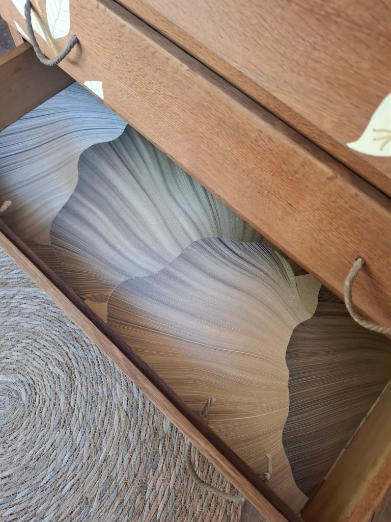 Tiroir en bois ouvert avec un fond en papier aux motifs ondulés dans des tons beige et marron.