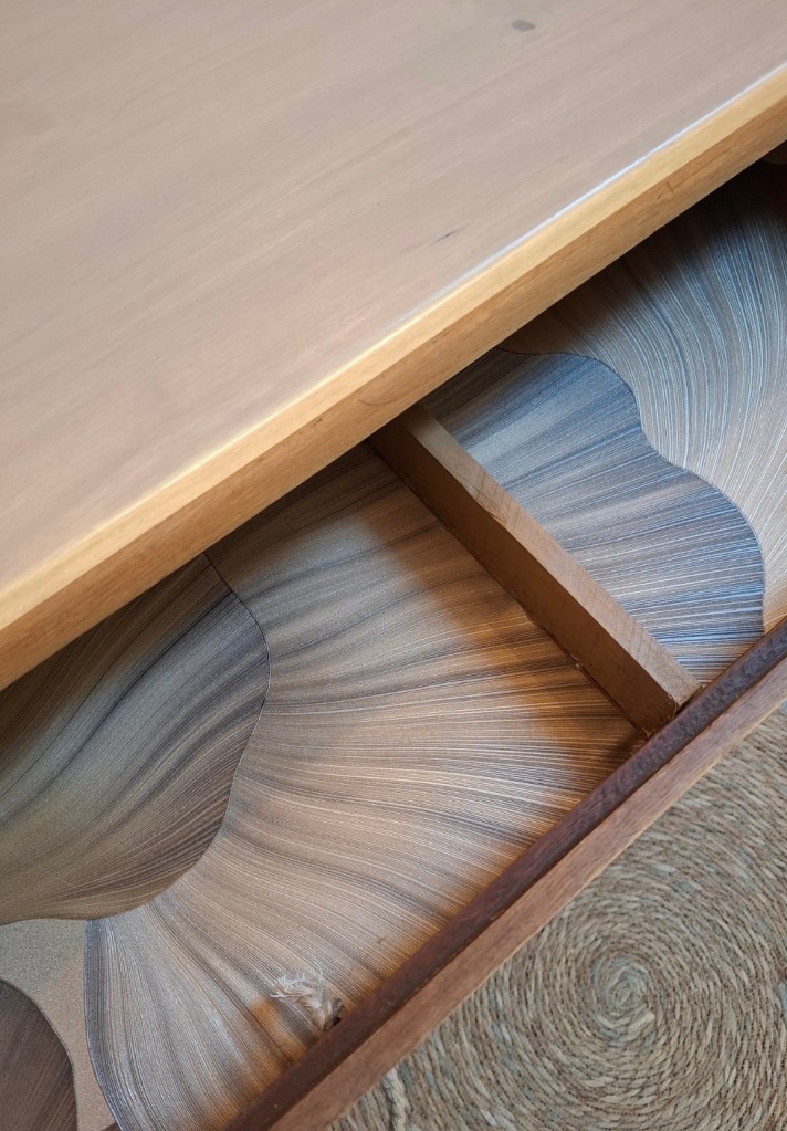 Plan de table en bois clair avec tiroir ouvert, montrant un intérieur aux motifs ondulés en beige et marron.