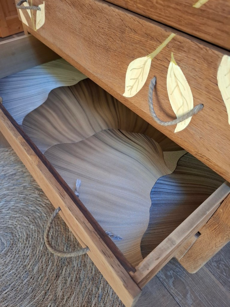 Tiroir en bois avec une finition intérieure ondulée et des motifs de feuilles peints sur le devant.