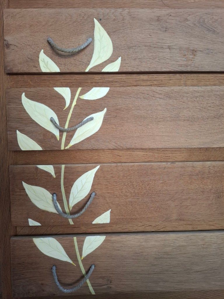 Tiroirs en bois avec des motifs de feuilles peintes et des poignées en corde.