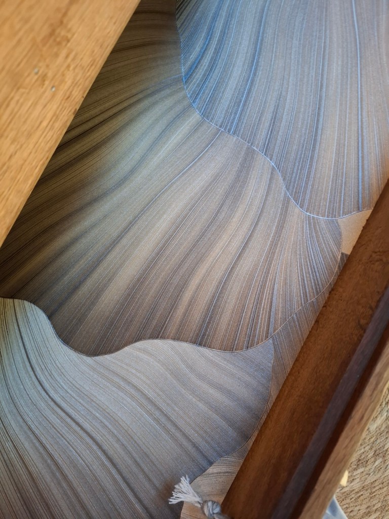 Vue rapprochée d'un design texturé en vagues de papier aux nuances de beige et bleu, encadré en bois.