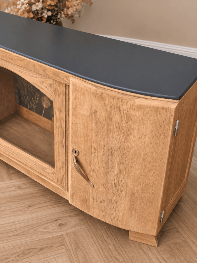Meuble en bois clair avec un dessus en métal noir, une porte vitrée et des détails floraux intérieurs.