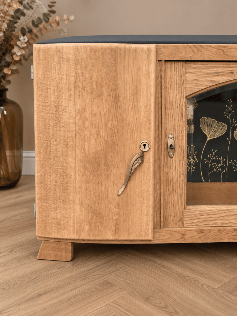 Un meuble en bois clair avec une porte en verre décoré, un bouton en forme de feuille et un fond noir.