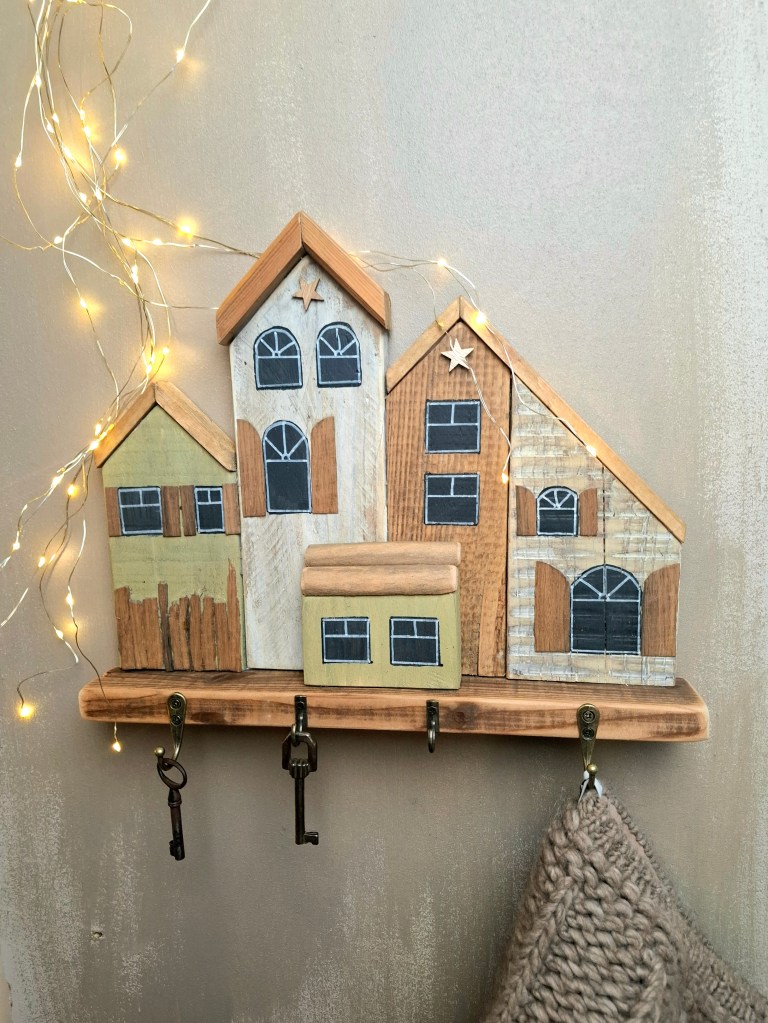 Porte-clés mural en forme de maisons en bois, décoré de lumières LED dorées.