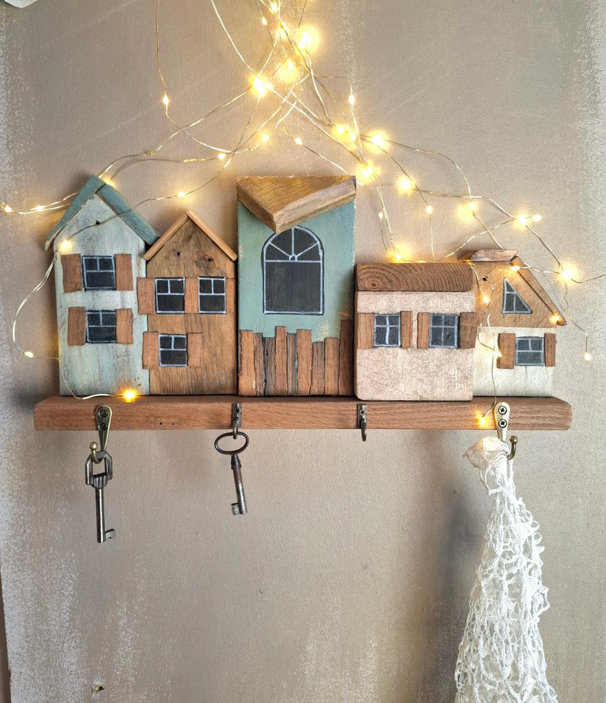 Décoration murale composée de maisons en bois coloré avec des lumières guirlandes, accroches pour clés en bas.