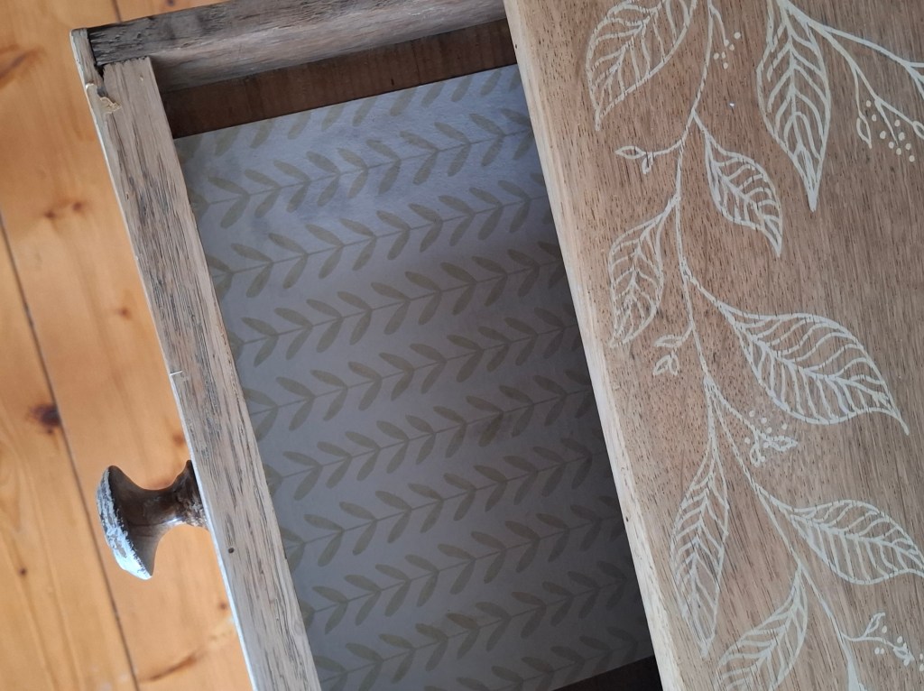 Tiroir en bois avec un motif de feuilles gravé sur le dessus et un fond à motif de feuilles dans l'intérieur.