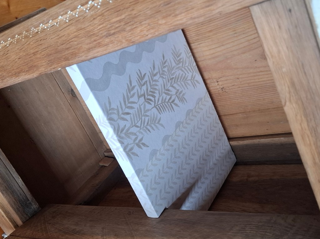 Un coin d'une pièce montrant une toile décorée de motifs de feuillage, positionnée à l'intérieur d'un meuble en bois.