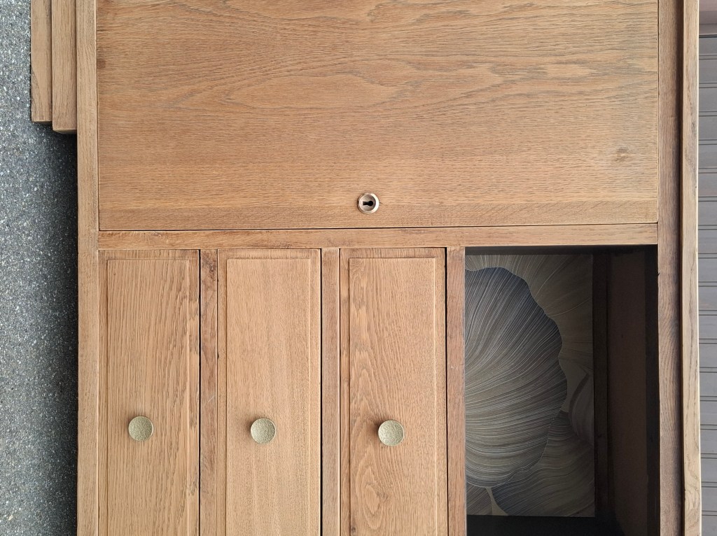 Meuble en bois clair avec deux tiroirs et trois portes, présentant un fond décoratif à l'intérieur d'une des sections.