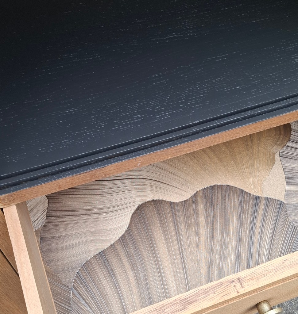 Dessus d'une commode noire en bois avec un tiroir ouvert, révélant un intérieur aux motifs ondulés en bois clair.