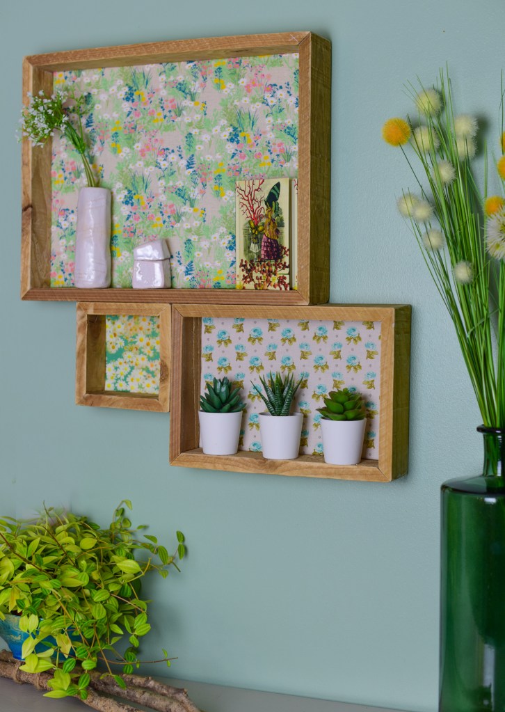 Étagères en bois avec des motifs floraux, contenant des plantes succulentes en pots blancs et des décorations.