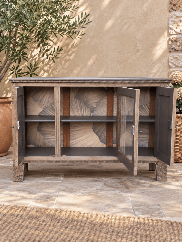 Buffet en bois avec deux portes vitrées, intérieur décoré de motifs ondulés, placé dans un environnement extérieur avec des plantes.